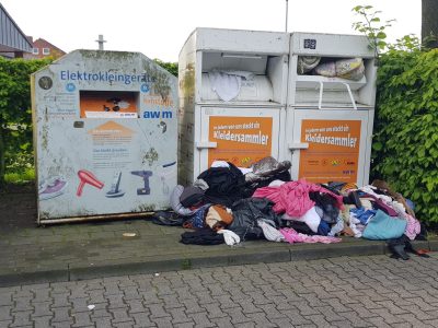Dieses Bild zeigt die überfüllten Altkeiderkontainer am Merkureck in Hiltrup mit einem großen Berg Kleider aussen davor.