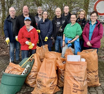 10 Menschen mit Müllzangen und Handschuhen an stehen hinter vollen Müllsäcken.